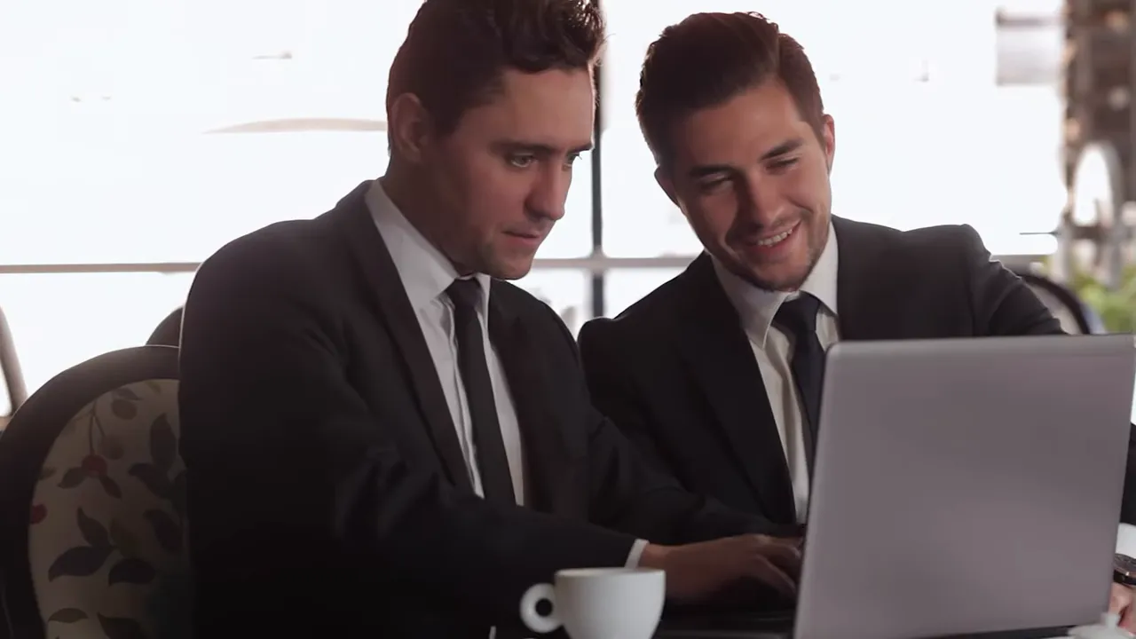 Two professionals in suits reviewing information on a laptop together in a meeting