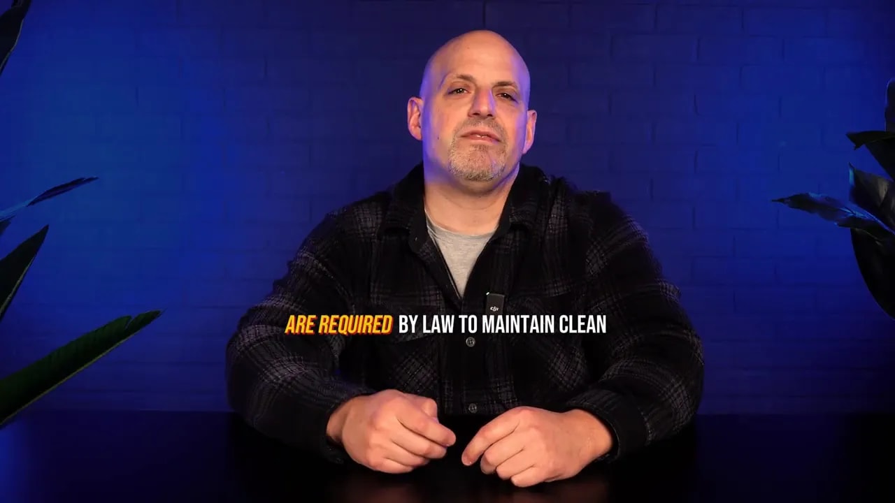 Presenter seated at desk in blue-lit studio with on-screen text 'ARE REQUIRED BY LAW TO MAINTAIN CLEAN' across the center