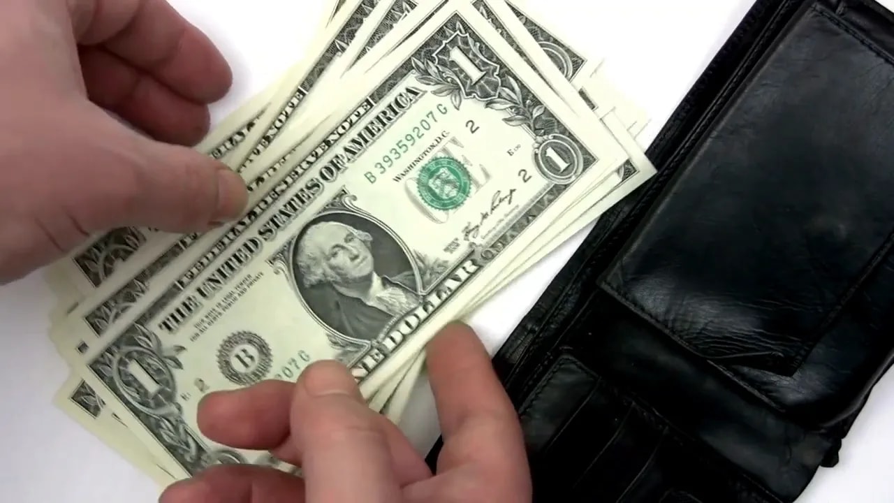 Hands counting United States dollar bills beside a black wallet