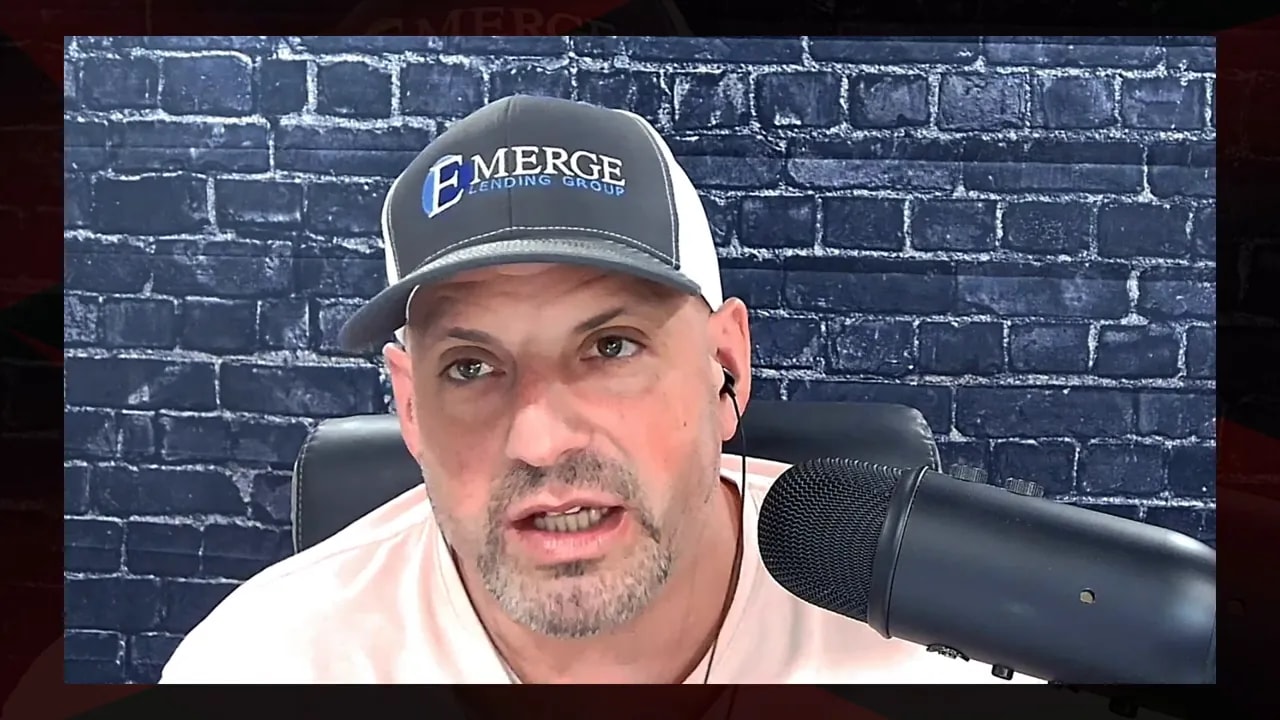 Alex Rosy speaking in front of a microphone against a brick wall backdrop while wearing an Emerge Lending Group cap