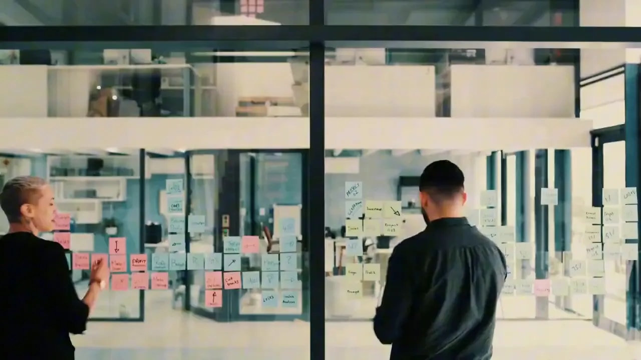 Two professionals reviewing planning notes on a glass wall