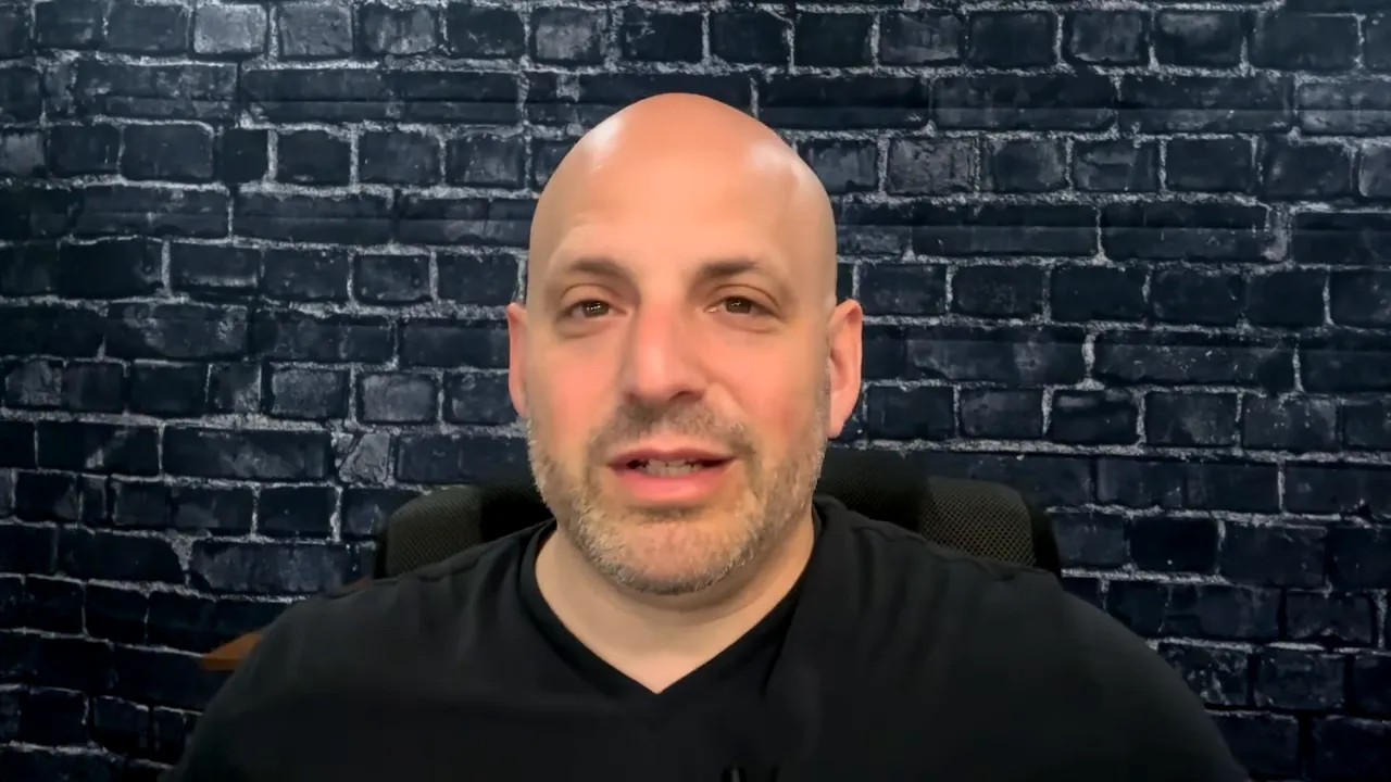 Head-and-shoulders shot of the podcast host centered against a dark brick wall, speaking to camera.