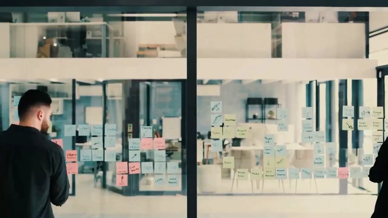 Two people discussing notes on a glass wall in an office