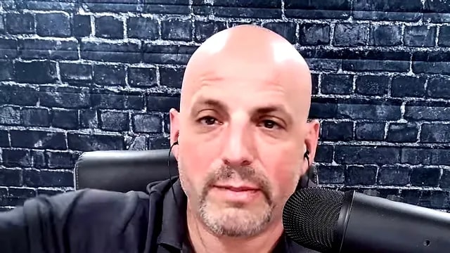 Presenter speaking into microphone against a brick wall background