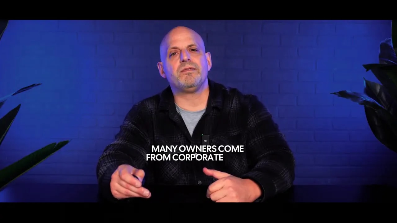 Host centered in a blue-lit studio with on-screen text 'MANY OWNERS COME FROM CORPORATE'.