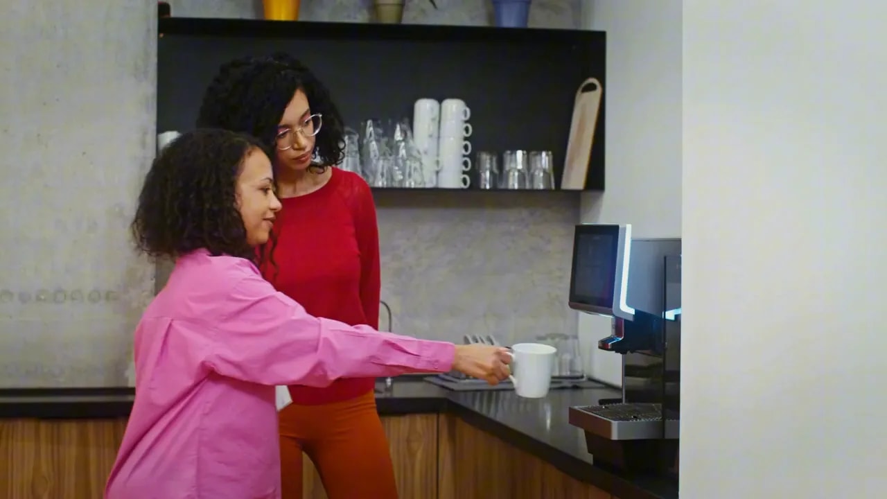 two women using an office coffee machine in a break room