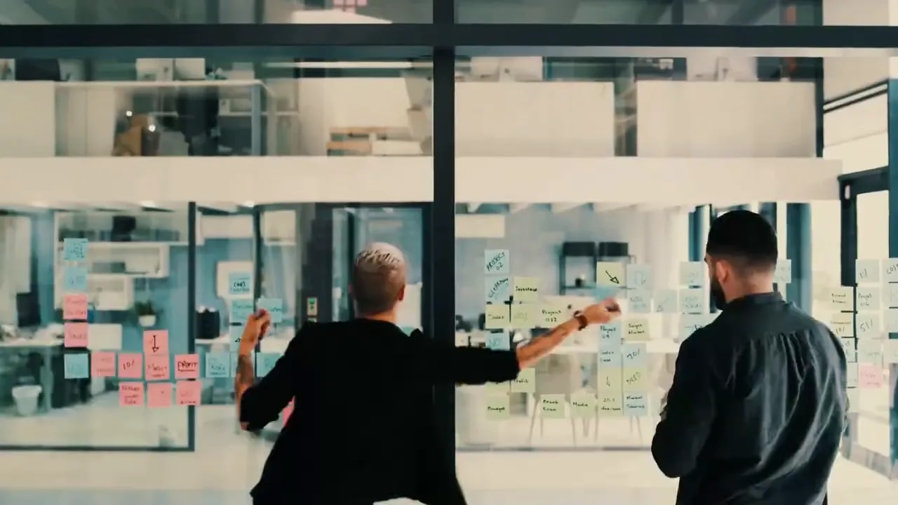 Two professionals standing in an office near a glass planning wall