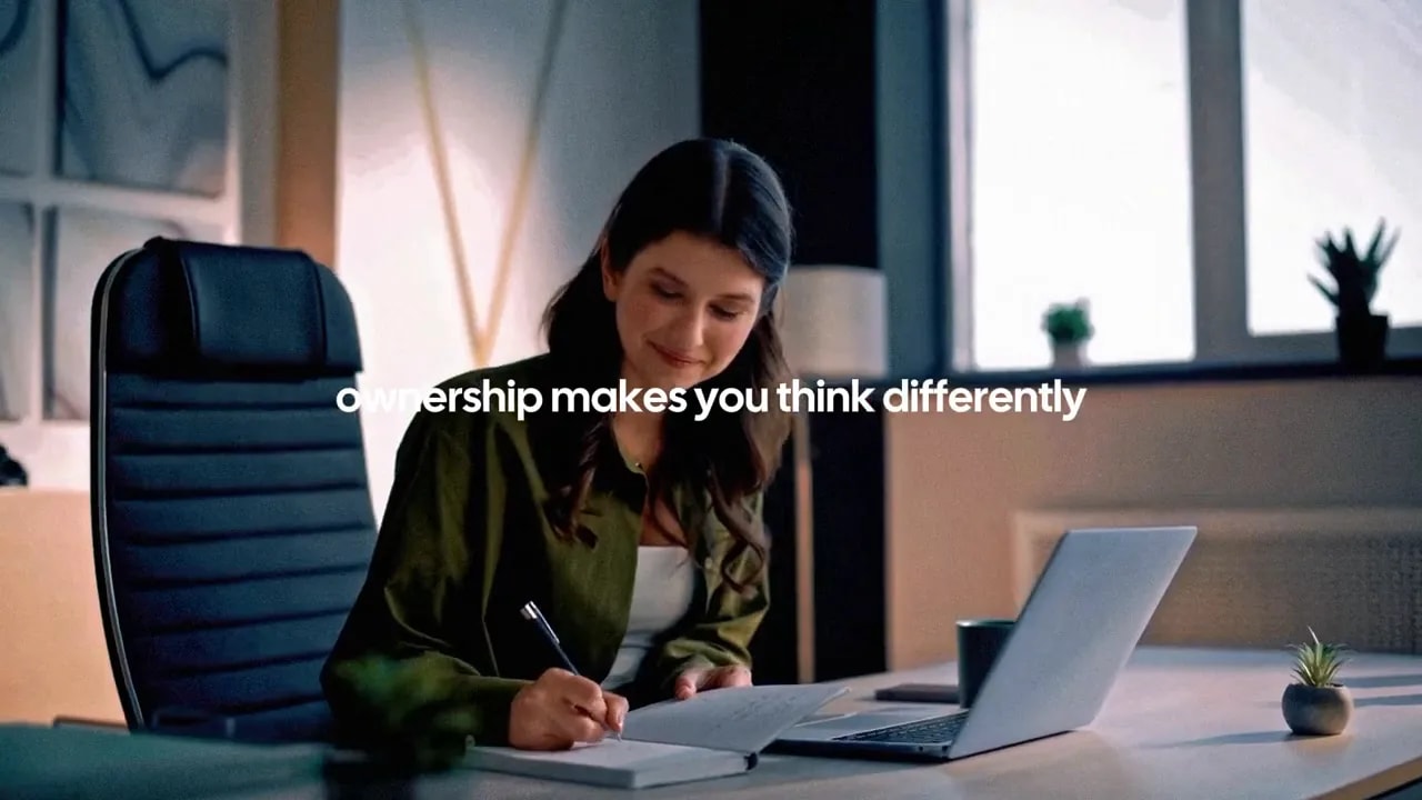 Woman working at a desk with laptop and notebook with the text 'ownership makes you think differently'