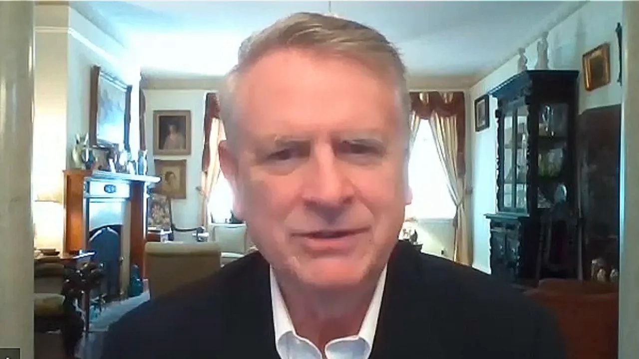 Crisp head-and-shoulders screenshot of a podcast guest on a video call with a living-room background.