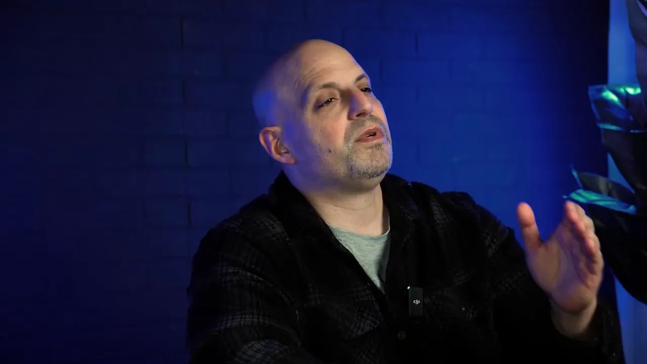 Speaker gesturing while outlining practical next steps in a blue-lit studio, clear and unobstructed.