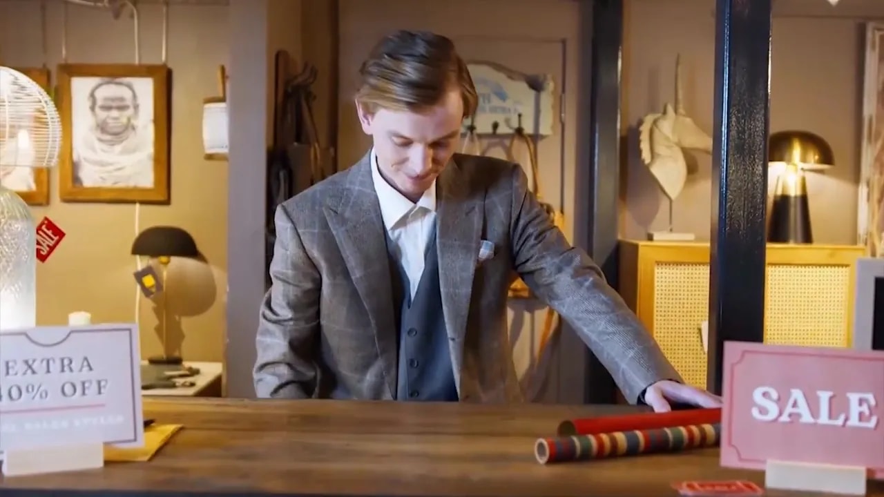 Retail store owner behind a counter with sale signage and wrapping paper rolls visible