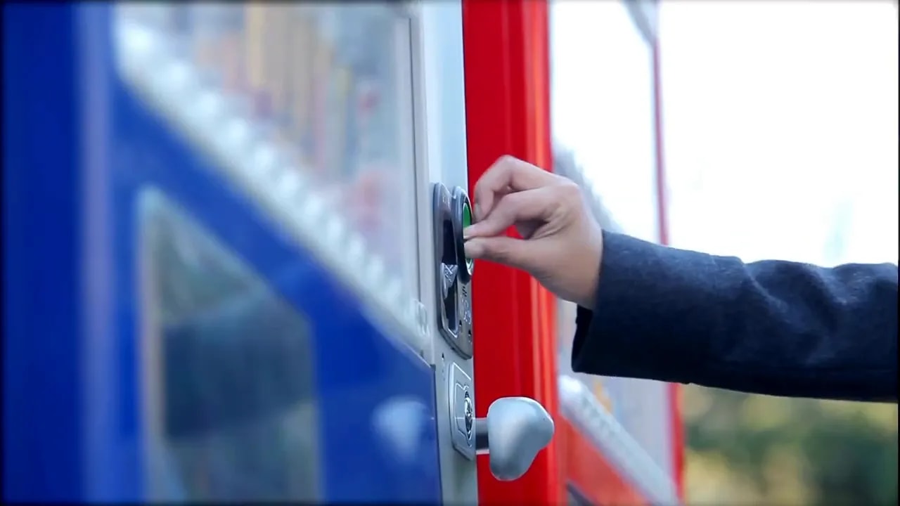 Hand pressing a button on a blue vending machine